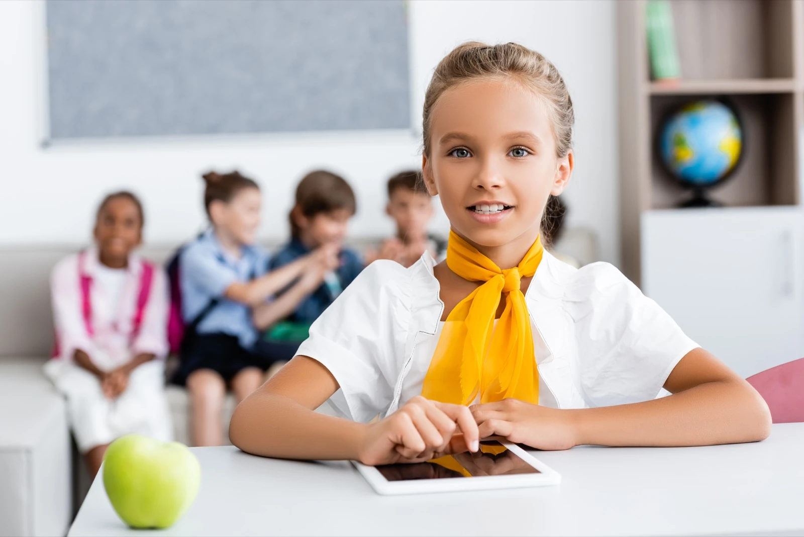 Schülerin mit Tablet im Klassenzimmer, selbstständiges Arbeiten, Mitschüler:innen im Hintergrund.